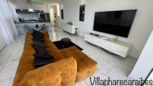 a living room with a brown couch and a flat screen tv at VILLA PHARE CARAÏBES Guadeloupe in Le Moule