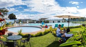a man and woman sitting under an umbrella by a pool at Guaduales del café a 403 in Montenegro