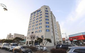 a tall building with cars parked in a parking lot at Hotel Grand Bay Boryeong in Boryeong