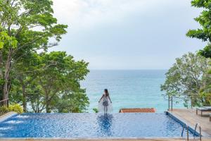Secret Cliff Resort & Restaurant - SHA Plus في شاطئ كارون: امرأة تقف على حافة مسبح مطل على المحيط