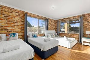 a bedroom with two beds and a brick wall at Absolute Blue by Experience Jervis Bay in Hyams Beach