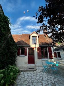 una casa con una puerta roja y dos sillas azules en Le Cottage des Chalands, en Saint-Georges-sur-Cher