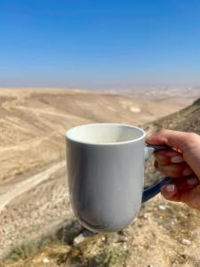 a person holding a cup of coffee in the desert at צימר בוטיק אדלה Zimmer boutique adela in Arad