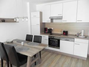 ヘリングスドルフにあるVilla Bettina - Ferienwohnung 02の白いキャビネット、木製テーブルと椅子付きのキッチンが備わります。