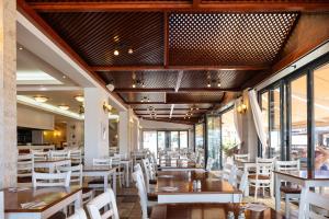 um restaurante com mesas, cadeiras brancas e janelas em Koni Village Hotel em Stalida