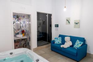 - un ours en peluche assis sur un canapé bleu à côté d'une baignoire dans l'établissement PALAZZO NICOLAUS del BORGO ANTICO, à Bari