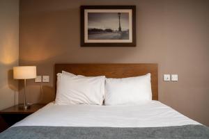 - un lit avec des draps blancs et une photo sur le mur dans l'établissement Wellington Hotel by Greene King Inns, à Aberdeen