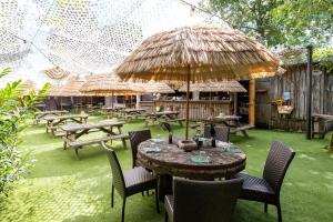un patio con mesas y sillas y una sombrilla de paja en Hôtel-Restaurant Logis l'Aubrac Laguiole, en Laguiole