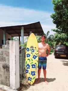 Um homem está ao lado de uma prancha de surf. em Exotic Beach Hotel em Arugam Bay