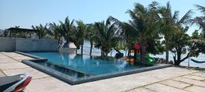 a swimming pool next to the water with palm trees at Myhoa Lagoon - Kiting Town in Phan Rang–Tháp Chàm