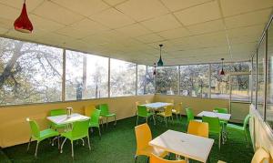 Kanari Mussoorie by Red Finch Hotels في موسوري: غرفة طعام مع طاولات وكراسي ونوافذ