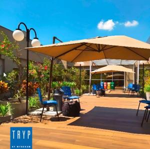 a patio with an umbrella and chairs and tables at TRYP BY WYNDHAM S&atilde;o Paulo Airport - Hotel de Transito Terminal 3 -Lado Ar - &Aacute;rea restrita &aacute; passageiros j&aacute; embarcados - Piso 1 in Guarulhos