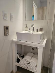 a white bathroom with a sink and towels on a shelf at Magnifique studio éco relaxant avec piscine in Mendoza