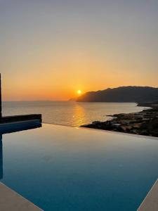 a sunset over the ocean with a swimming pool at Petra Nova Villas in Mochlos