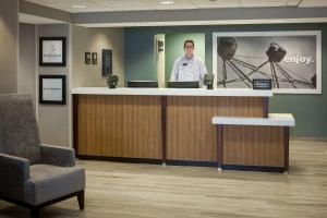 a man standing behind a counter in a waiting room at Hampton Inn Kansas City Liberty in Liberty