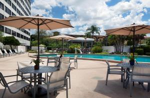 Hilton Tampa Airport Westshore في تامبا: فناء به طاولات ومظلات بجوار حمام سباحة