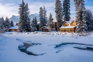 a house in the snow with a stream in front at Post Hotel & Spa in Lake Louise