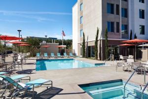 uma piscina com cadeiras e guarda-sóis ao lado de um hotel em Homewood Suites by Hilton Aliso Viejo Laguna Beach em Aliso Viejo