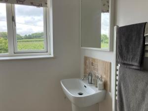 ein weißes Bad mit einem Waschbecken und einem Fenster in der Unterkunft Withy Farm in Canterbury