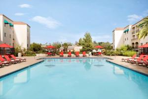 een zwembad in een hotel met rode stoelen en tafels bij Embassy Suites by Hilton Temecula Valley Wine Country in Temecula