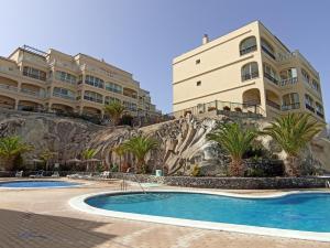 a building next to a swimming pool in front of a building at Golf del Sur Apartment - magnificent panorama of the ocean, el Teide, and Montaña Roja in San Miguel de Abona