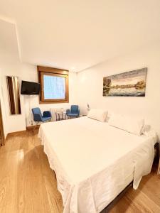 a bedroom with a large white bed and two chairs at Pensión Sarasate in Pamplona