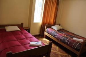 two beds in a room with red sheets and a window at Cuscopackers Hostels in Cusco