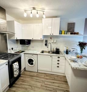 a kitchen with white cabinets and a sink and a stove at NKN cosy maisonette close to Dartford train station, free parking, food, shopping in Kent