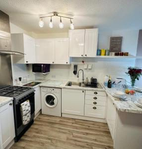a kitchen with white cabinets and a sink and a dishwasher at NKN cosy maisonette close to Dartford train station, free parking, food, shopping in Kent