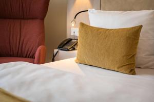 a bed with a yellow pillow and a telephone at First Inn Hotel Zwickau in Zwickau