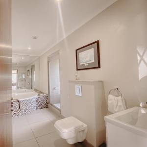 a white bathroom with a tub and a toilet and a sink at Sunset Villa in Langebaan