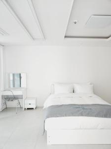 a white bedroom with a bed and a desk at Vesper Namhae in Namhae