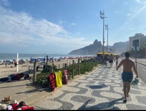 un hombre caminando por una acera junto a la playa en Duplex Ipanema Vinícius de Moraes, en Río de Janeiro