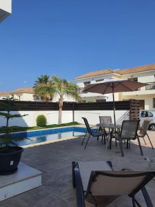 een patio met stoelen en een parasol naast een zwembad bij Yama's Villa - Polyxenia luxury, protaras, cyprus in Protaras