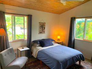 a bedroom with a bed and a chair and windows at Seaside House and Aloha Bungalow in Pahoa