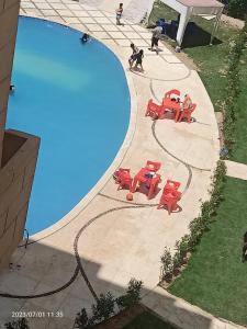 vistas a una piscina con mesas y sillas rojas en استديو مكيف ب ٦٥٠ اليوم ك ٨٤ قبلي أمام زهران والزهور, en Abû Zeira
