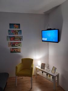 een woonkamer met een gele stoel en een televisie aan de muur bij Anja Apartman in Novi Sad