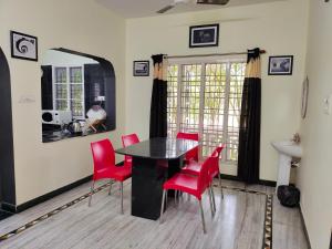 uma sala de jantar com uma mesa preta e cadeiras vermelhas em The Mahizh Home em Mahabalipuram