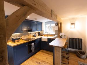 Il comprend une cuisine avec des placards bleus et du parquet. dans l'établissement Cotswold cottage with hot tub, à Bledington