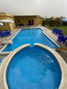 einem großen Pool mit blauen Stühlen und einem Gebäude in der Unterkunft تيوليب فيلا in Madinat as-Sadis min Uktubar