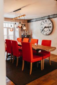 a dining room with a table and red chairs and a clock at Le Nid de la Canette in Durbuy