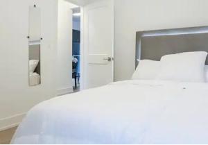 a white bedroom with a white bed and a mirror at Luxury Suite 4mins To Falls in Niagara Falls