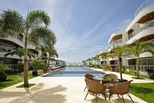 a resort swimming pool with chairs and a table and palm trees at Dunas de Cotovelo in Parnamirim