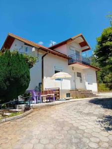 Cette maison dispose d'une terrasse avec des chaises violettes et un parasol. dans l'établissement Gemütliches Ferienhaus in Elsani, à Elshani