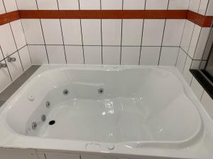 a white bath tub in a bathroom with white tiles at 24 Horas Motel Jaguar Contagem in Contagem