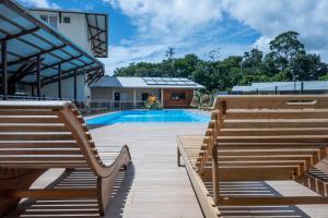 a swimming pool with two wooden benches next to a building at Hôtel Belle Terre Resort in Macouria
