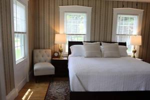 a bedroom with a bed and a chair and two windows at Hillside Haven: Luxe Farm Escape - 5BR-2 King Beds in Swanzey