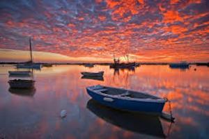 a boat sitting in the water with a sunset at The retreat in West Mersea