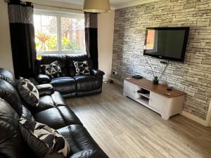 a living room with a leather couch and a flat screen tv at Tidy 3 bedroom property within St Andrews. in Fife