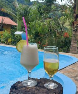 two glasses of drink on a table next to a pool at Recanto Casa Amarela de São Romão in Nova Friburgo
